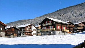 A row of wooden cabins with balconies, set against a snowy mountain backdrop. - Heiderösli by Interhome (Grächen)