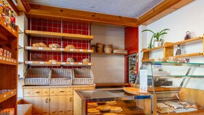 Una panadería con estantes de madera que exhiben pan y pasteles, un mostrador con pasteles y una barra con un menú.