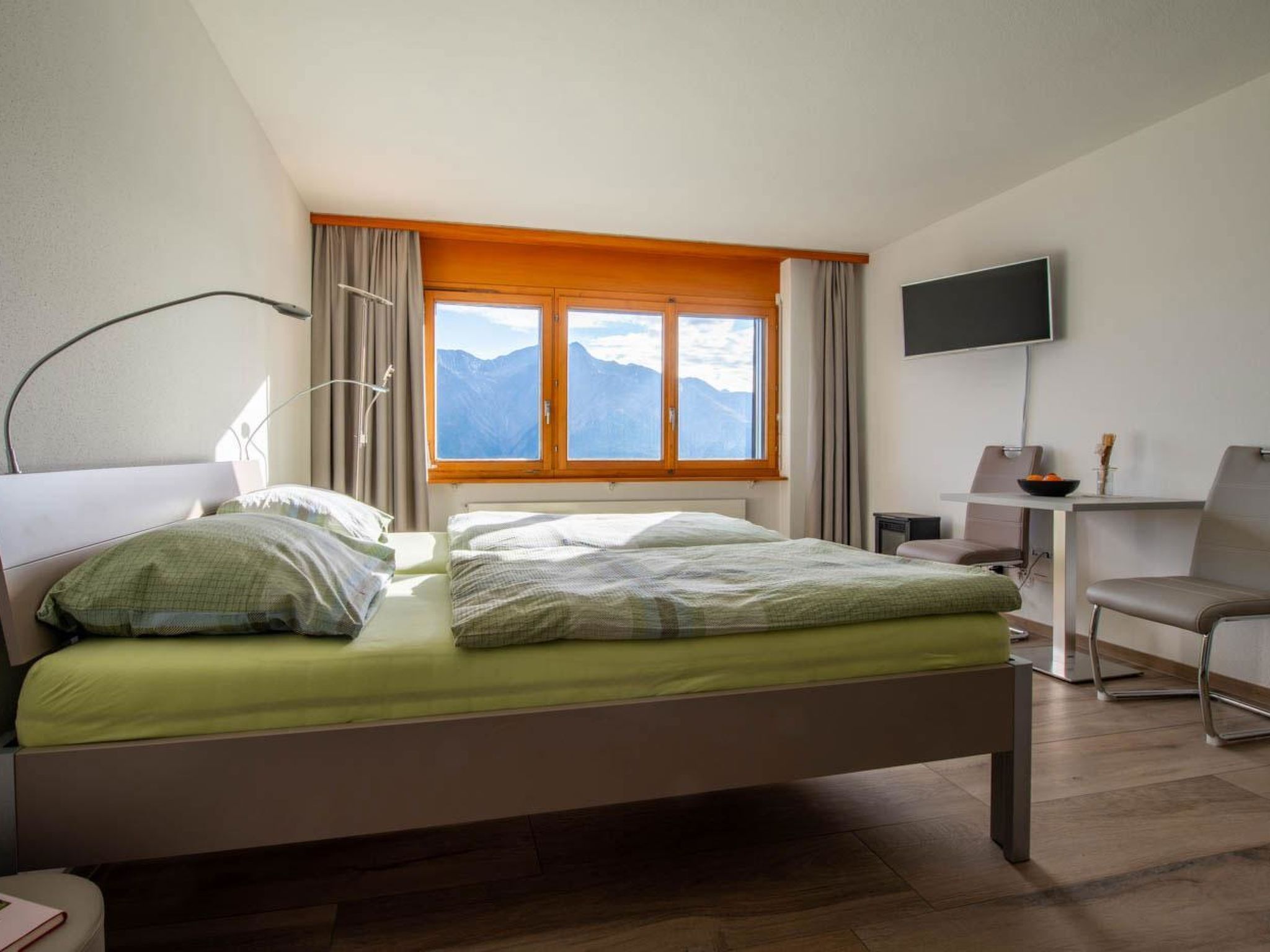 A hotel room with a bed, a desk, a chair, a TV, and a window with a mountain view.