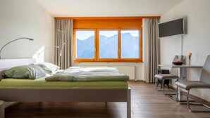 Un dormitorio con cama, escritorio, silla, televisor y ventana con vista a la montaña.