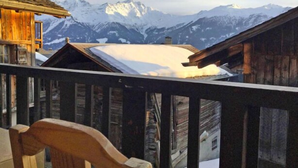 En træchalet med balkon med udsigt over sneklædte bjerge.