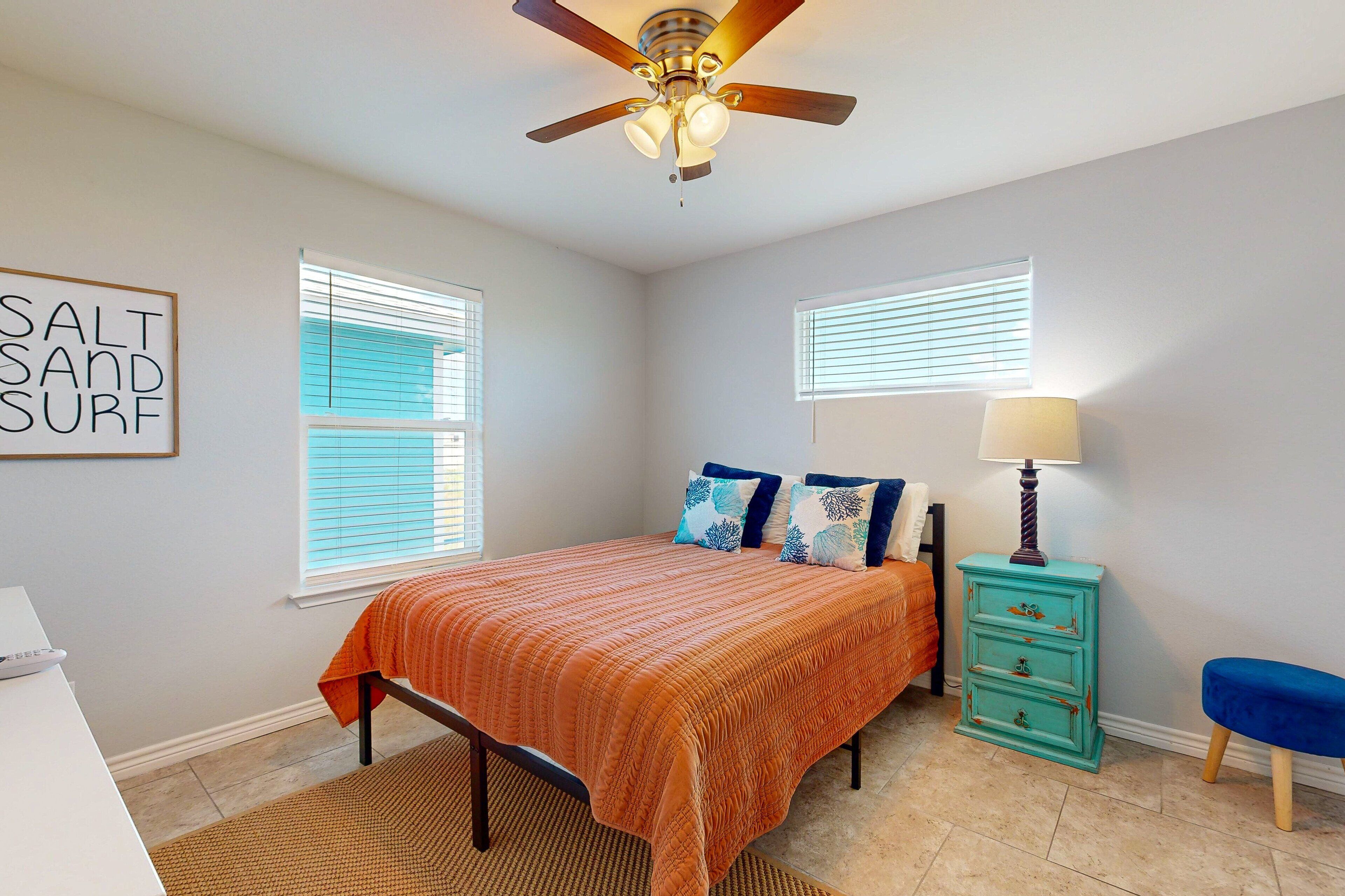 A bedroom with a bed, a ceiling fan, a dresser, a lamp, and a wall sign.