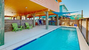 A pool area with green Adirondack chairs, a covered seating area, and a wooden deck. - FC1702 Private Heated  Pool, Room for Boat Parking, Golf Cart Included (Port Aransas)