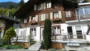 Un chalet à deux étages avec une façade en bois, de nombreuses fenêtres dotées de volets et un balcon agrémenté de jardinières.
