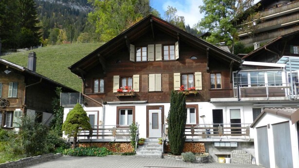 Un bâtiment de style chalet traditionnel, doté d’une façade en bois, de nombreuses fenêtres avec volets et d’un balcon agrémenté de jardinières.