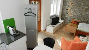 Une pièce compacte comprenant un coin cuisine, un lit, une télévision et un mur en pierre.