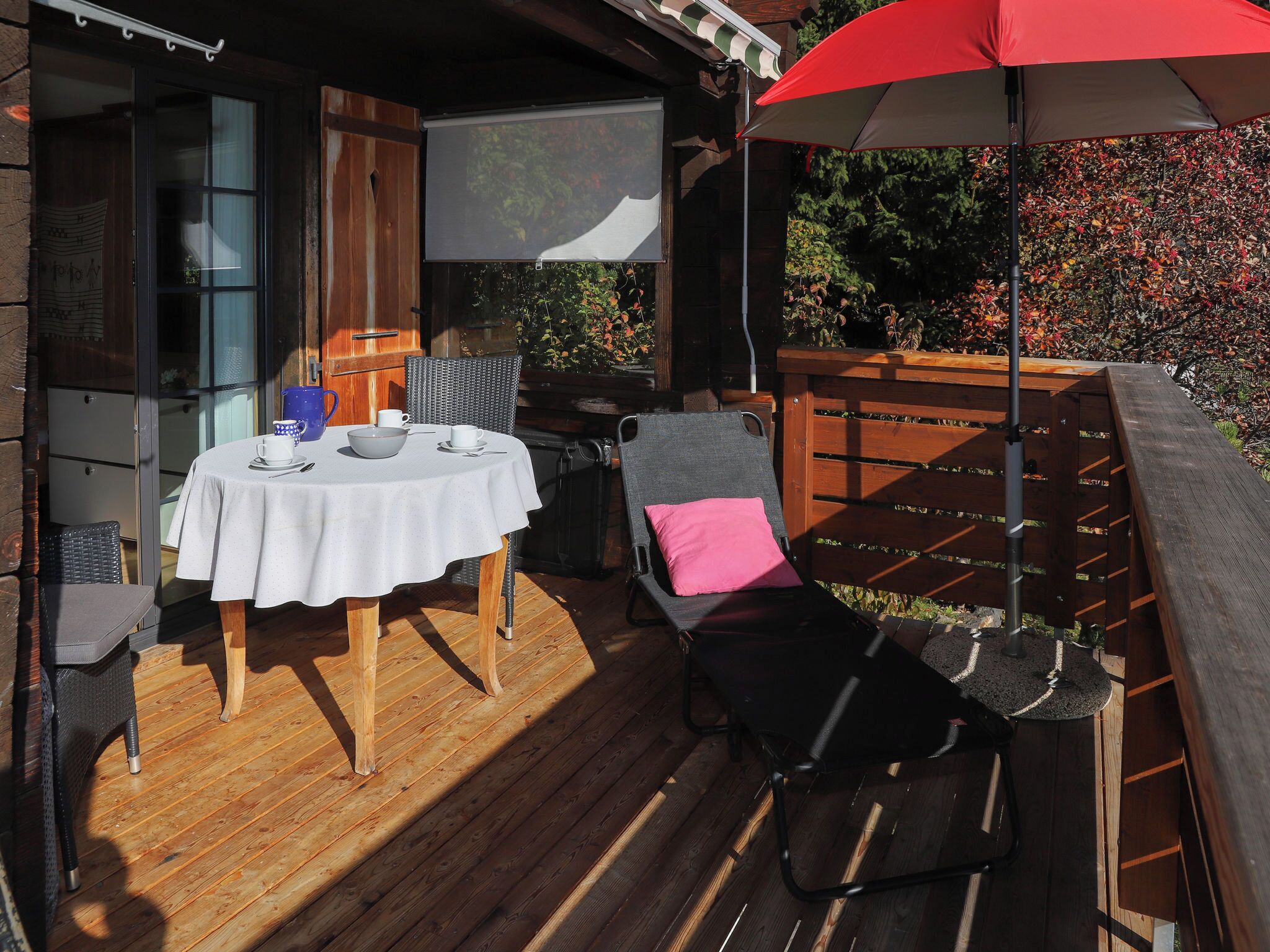 An outdoor patio with a round table, chairs, and a red umbrella.