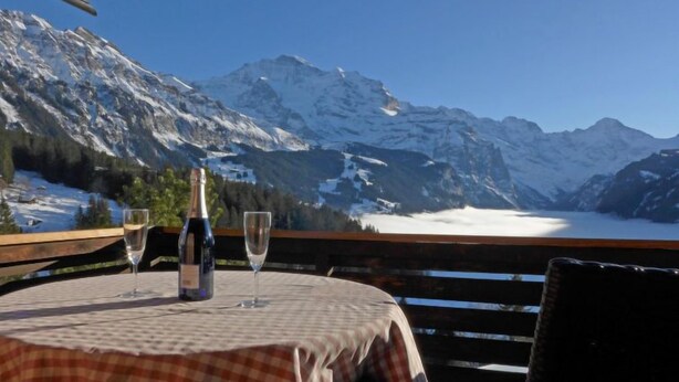 A table with a bottle and two glasses, set against a backdrop of snow-capped mountains and a lake. - Jungfrau a d Ledi by Interhome (Wengen)
