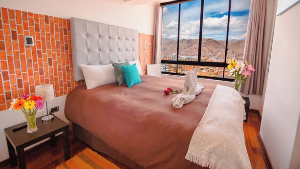 A hotel room with a large bed, a view of a cityscape, and a brick-patterned wall.
