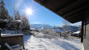 A snowy outdoor area with a wooden deck and a view of snow-covered mountains.
