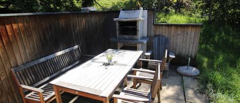Una terraza de madera con una mesa y bancos, rodeada por una valla de madera y una parrilla.