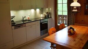 Una cocina con armarios blancos, encimera negra, un fregadero y una mesa de comedor de madera con un frutero.