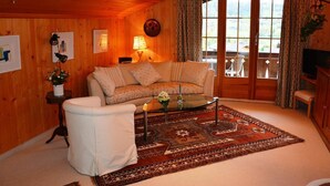 Una sala de estar acogedora con paredes de madera, un sofá, un sillón blanco, una mesa de centro y una alfombra estampada.
