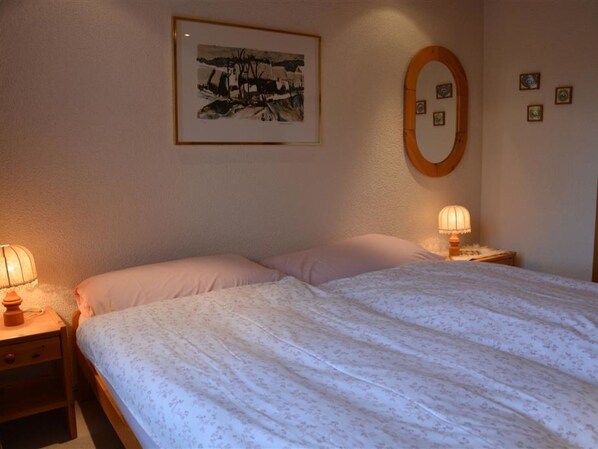 A bedroom with a bed, two bedside tables, a wall-mounted mirror, and a framed picture.