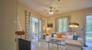 A living room with a white sofa, a glass coffee table, a ceiling fan, and a TV on a wooden stand. - Villetta Arcobaleno - with lake view and pool (Bardolino)