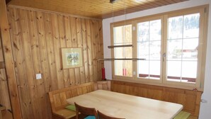 Una habitación con paneles de madera, una mesa grande y bancos, una ventana con vistas a un paisaje nevado y un cuadro en la pared.
