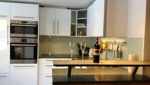 Una cocina moderna con armarios blancos, electrodomésticos de acero inoxidable y una botella de vino en la encimera.
