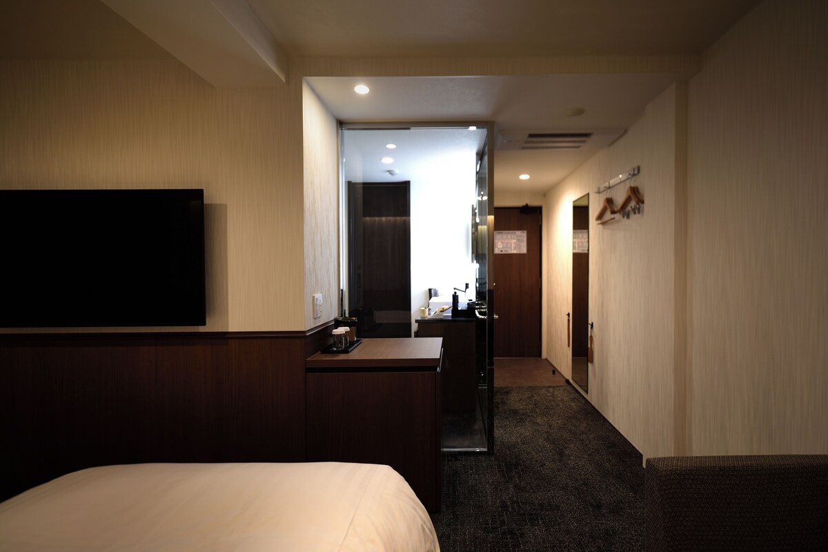 A hotel room with a bed, a desk, a flat-screen TV, and a kitchenette.