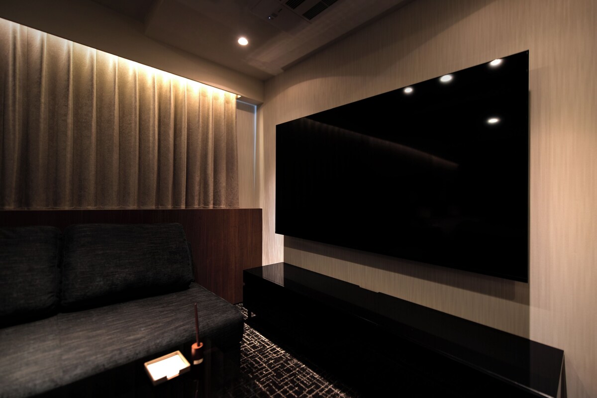 A modern living room with a large flat-screen TV mounted on the wall, a dark-colored sofa, and a wooden accent wall.