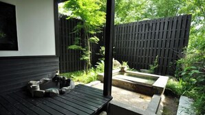 A wooden deck with a stone basin and a small pond, surrounded by a wooden fence and greenery. - Futarishizuka (Kirishima)