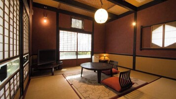 Una habitación japonesa tradicional con suelo de tatami, una mesa baja con cojines, un televisor y puertas correderas shoji.