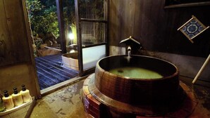 A wooden bathtub in a room with a window, a tiled floor, and a small shelf with bottles. - Futarishizuka (Kirishima)