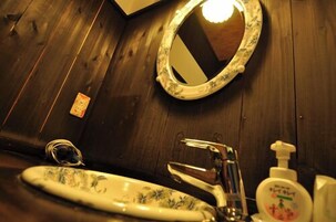 Un baño con pared de madera, un espejo redondo, un lavabo con diseño floral, un grifo y un dispensador de jabón.