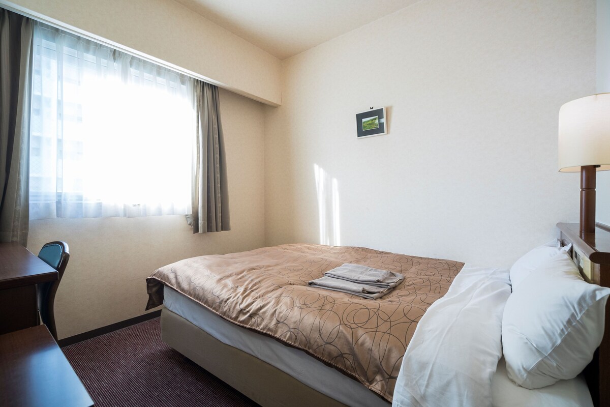 A hotel room with a bed, a desk, and a lamp.