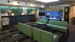A hotel lobby with a reception desk, green seating area, and a TV screen.
