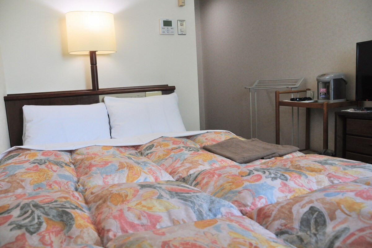 A hotel room with a bed, a bedside table with a lamp, a television, and a coffee maker.