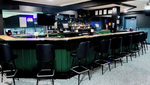 Un espace bar avec un comptoir, des tabourets et un écran de télévision.
