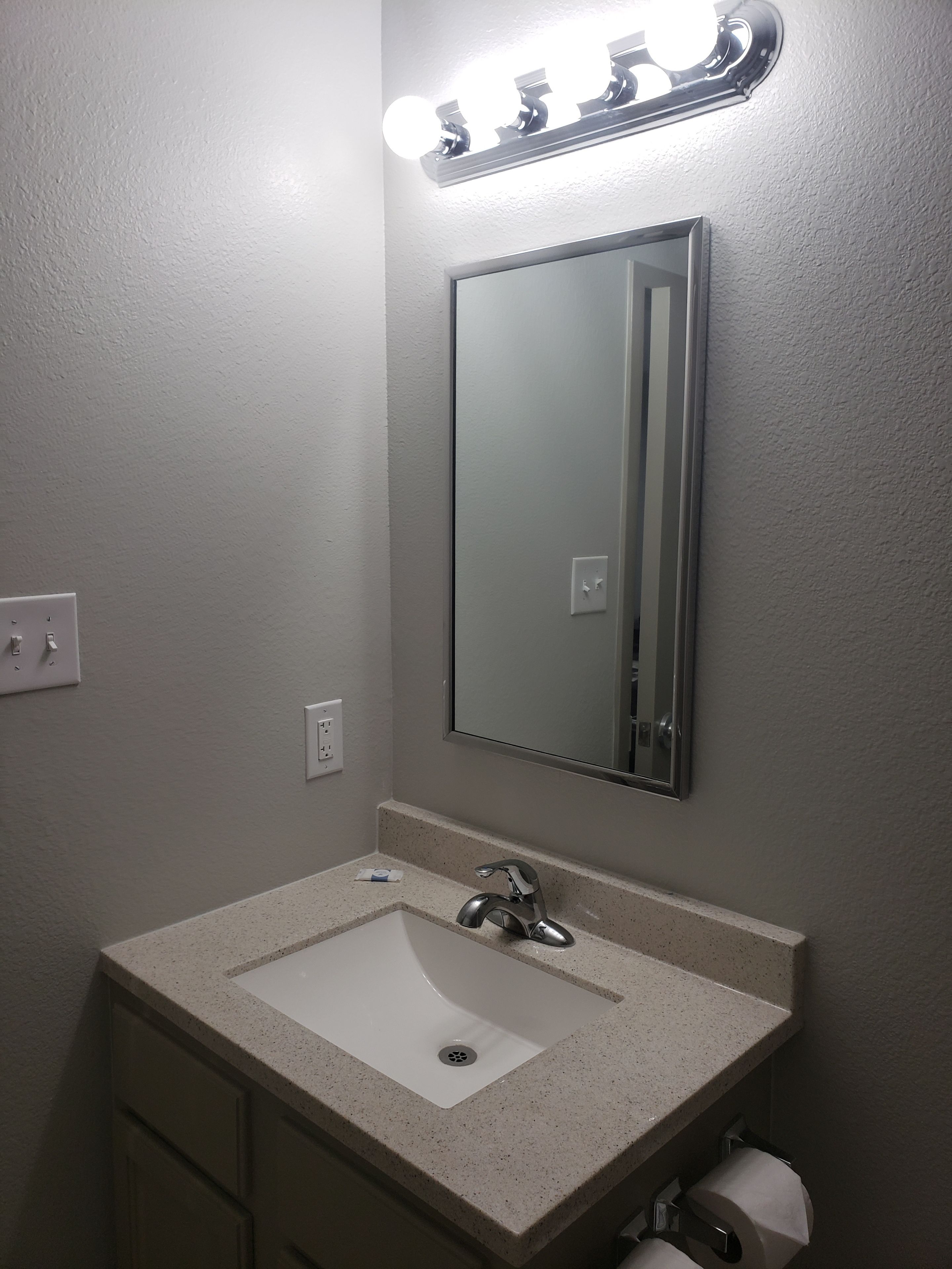 Un baño con lavamanos blanco, espejo y dispensador de papel higiénico.