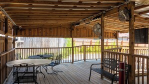 Une terrasse en bois avec une table et des chaises, un banc et un ventilateur.