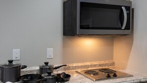 Une cuisine équipée d’un four à micro-ondes, d’une cuisinière, de casseroles, de poêles et d’un torchon blanc posé sur le plan de travail.