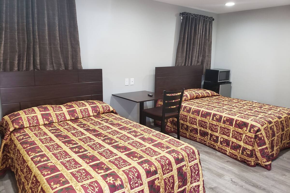 A hotel room with two beds, a desk, a chair, and a TV.
