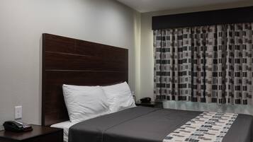 Habitación de hotel con una cama grande, cabecera de madera, mesita de noche con un teléfono y cortina estampada.