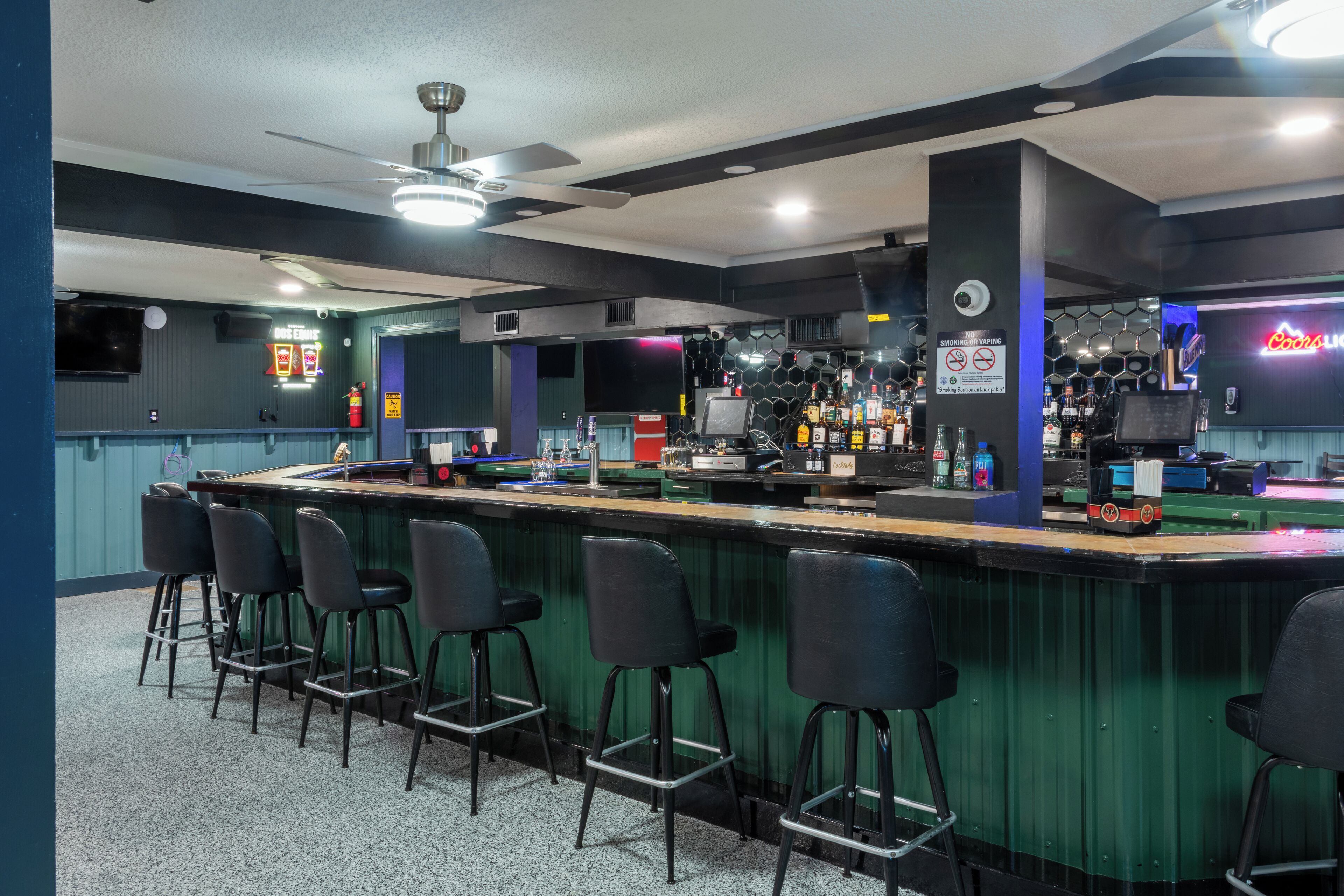 Een bar met een toonbank, krukken en verschillende flessen en glazen.