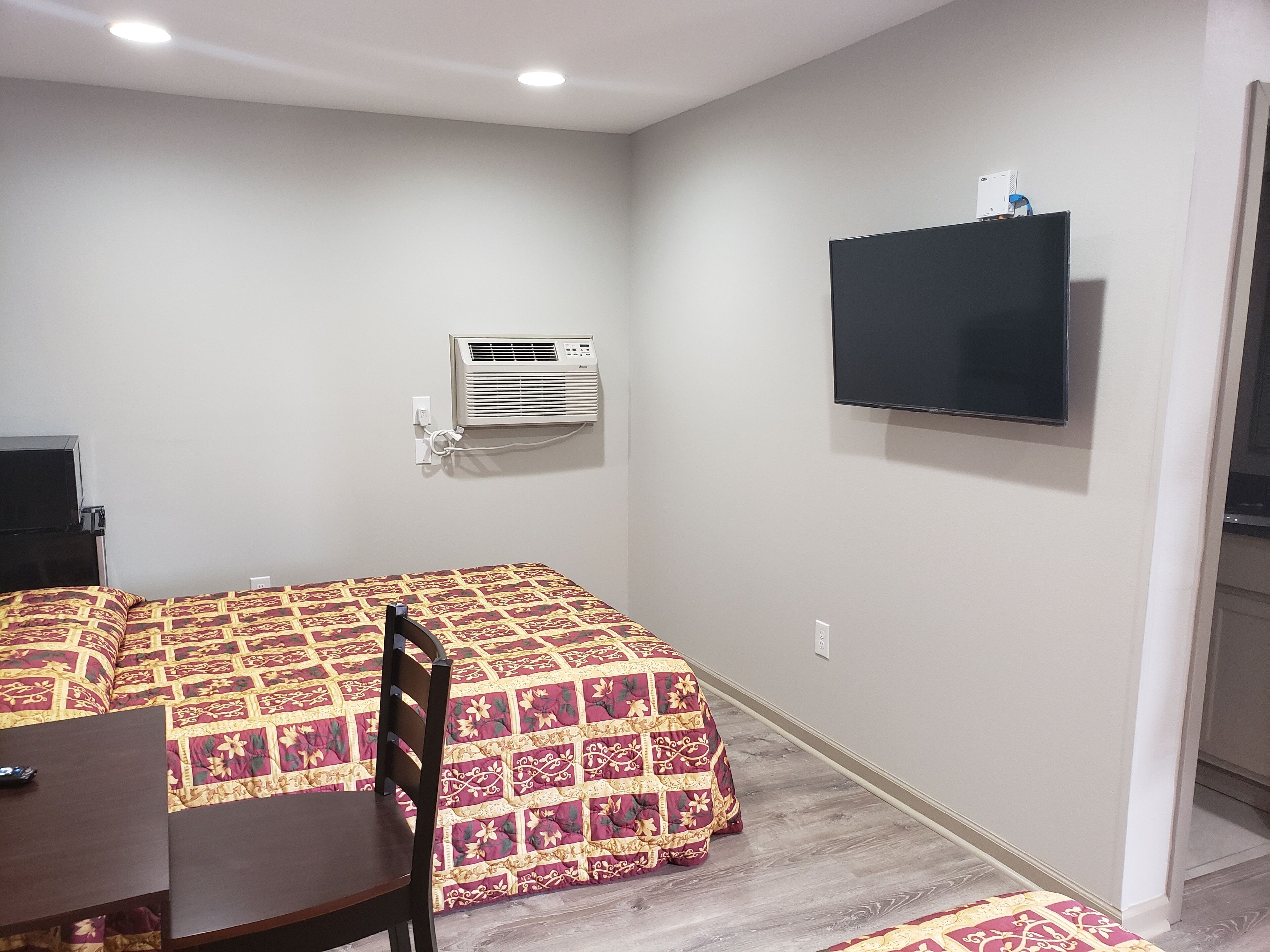 Quarto de hotel com uma cama, uma mesa de escritório, uma cadeira, ar condicionado e uma televisão na parede.