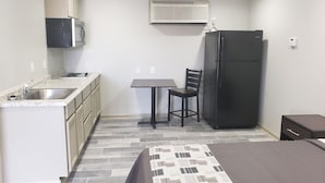 Une petite cuisine équipée comprenant un évier, une cuisinière et un four à micro-ondes, une petite table avec une chaise, un réfrigérateur et un lit avec une couvre-lit à motifs.