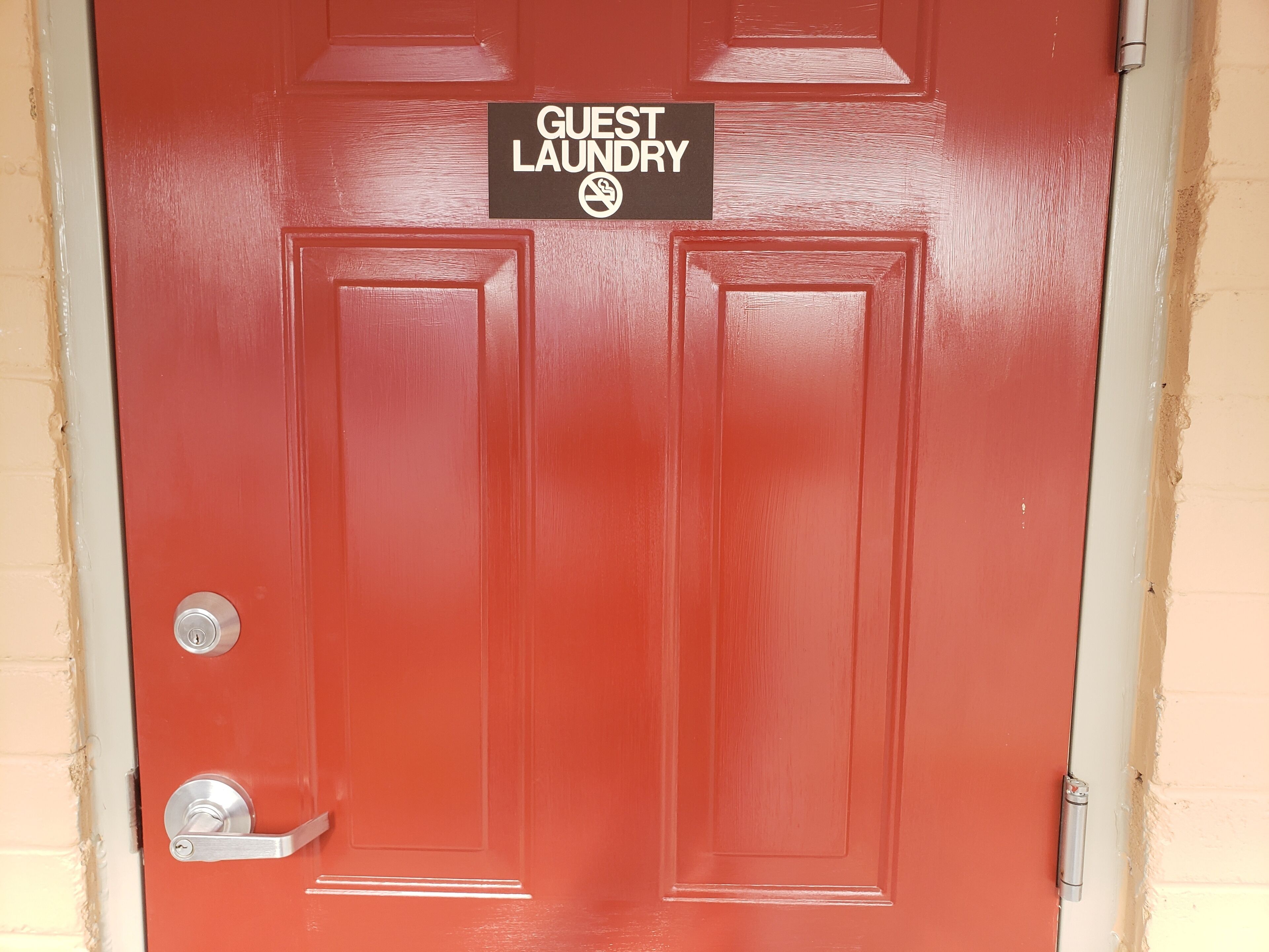 En rød dør med et skilt, der står "Guest Laundry", og et symbol for rygning forbudt.