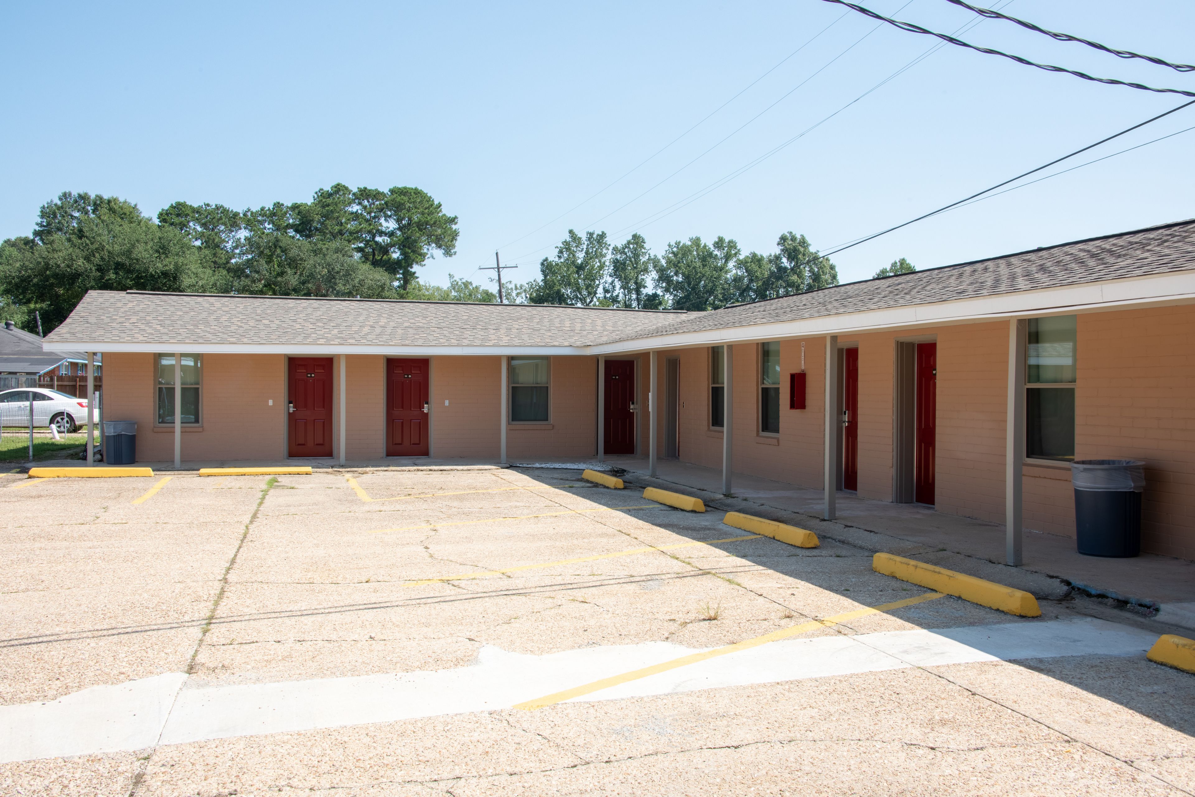 A motel with a parking lot, multiple rooms with red doors, and a simple, functional design.