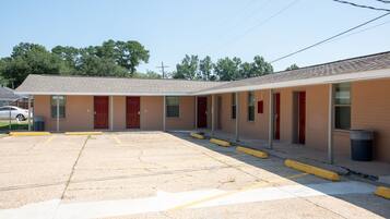 A motel with a parking lot, multiple rooms with red doors, and a simple, functional design.