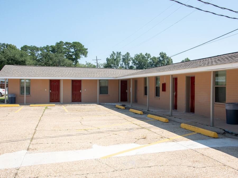 A motel with a parking lot, multiple rooms with red doors, and a simple, functional design.