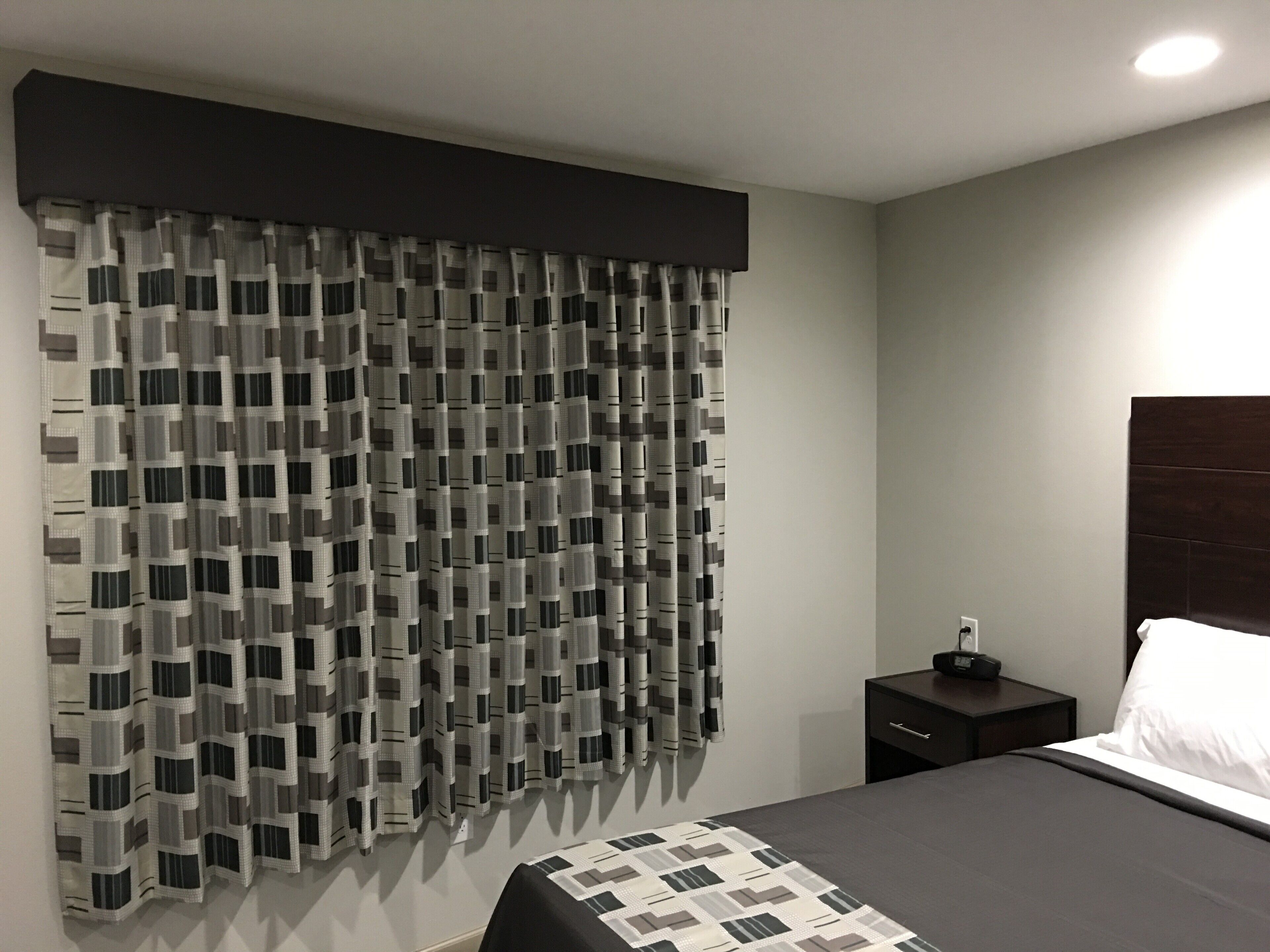 Une chambre à coucher avec un grand lit, une table de chevet, une tête de lit sombre et un rideau à motifs.