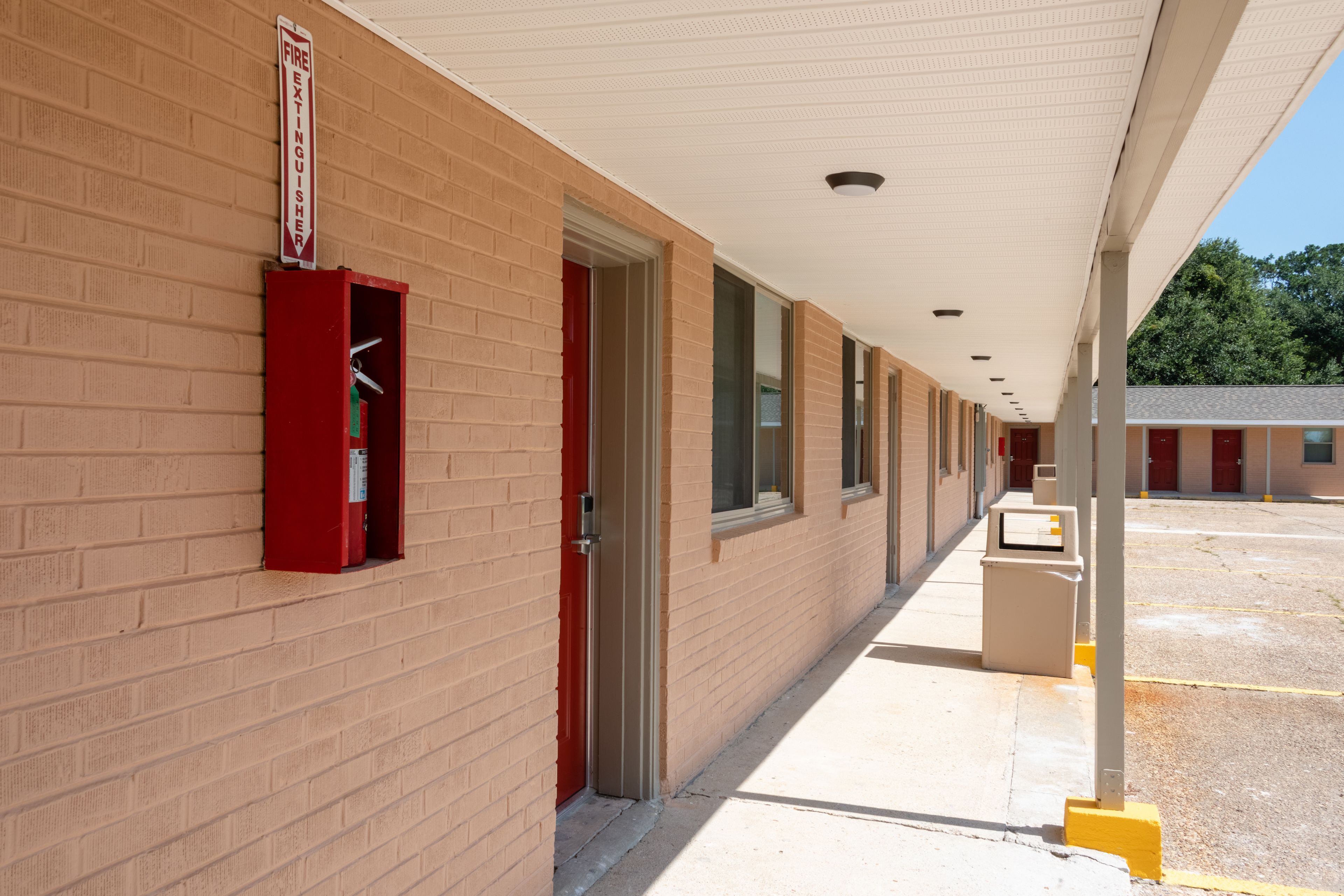 A building with a fire extinguisher mounted on the wall, a covered walkway, and a parking area.