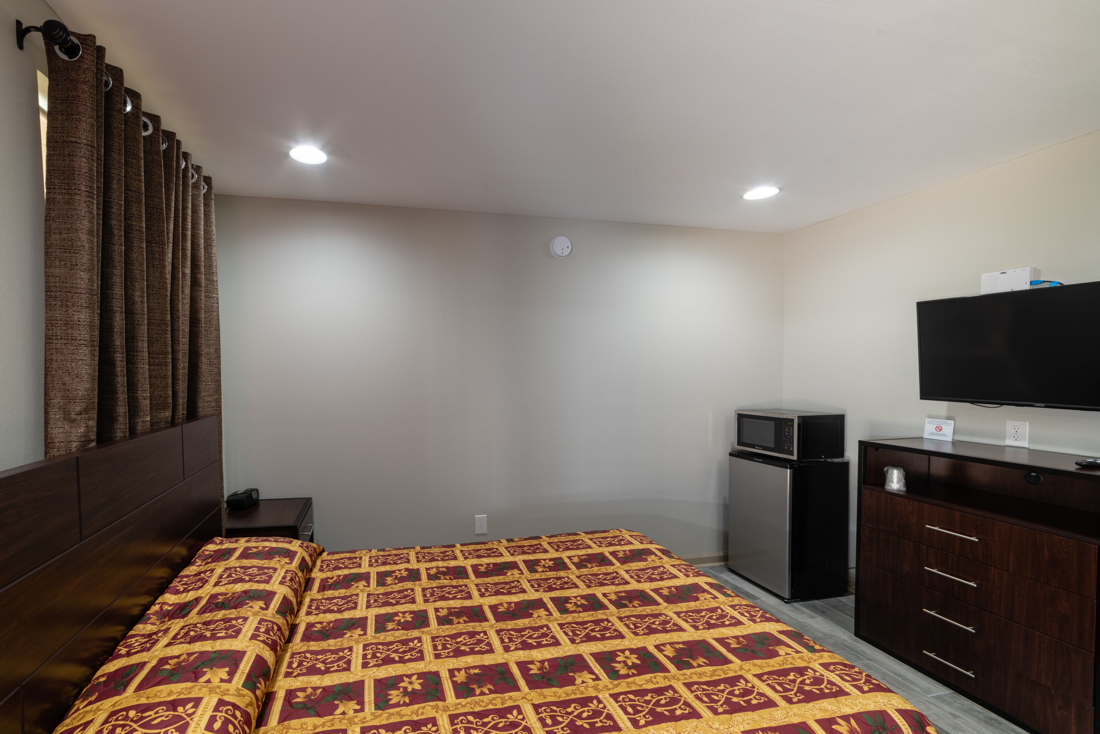 Una habitación de hotel con cama, televisor, mini refrigerador y cómoda de madera oscura.
