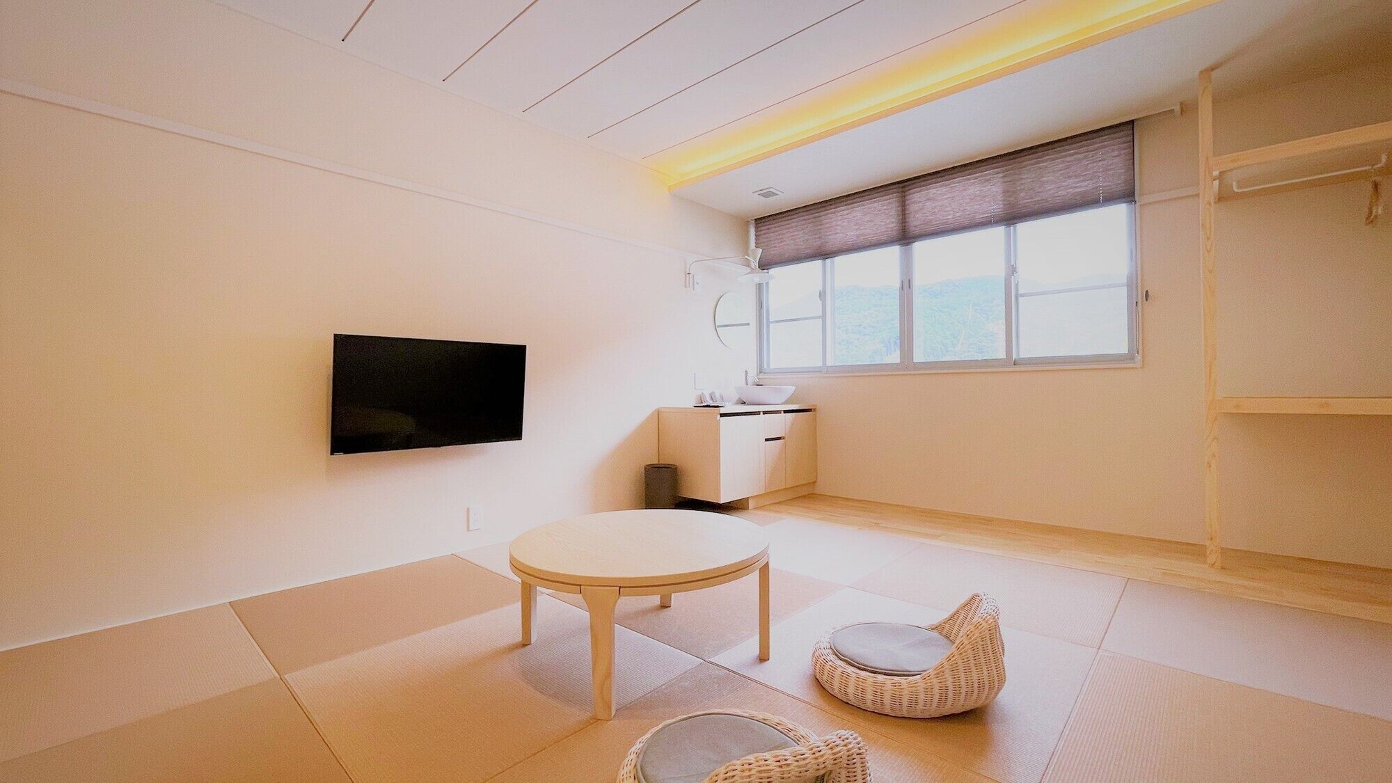 A minimalist room with a TV, a small table, a wicker chair, and a window with a view.