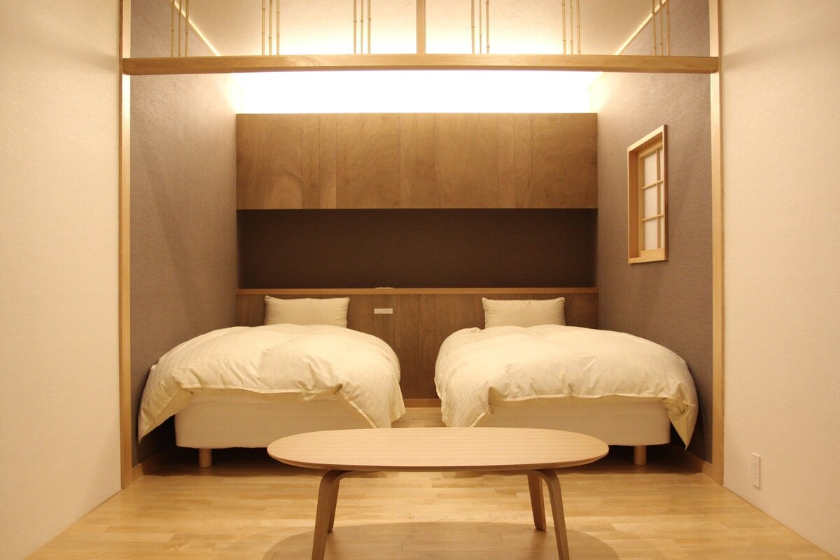 Una habitación pequeña con dos camas, una mesita y un cabecero de madera.