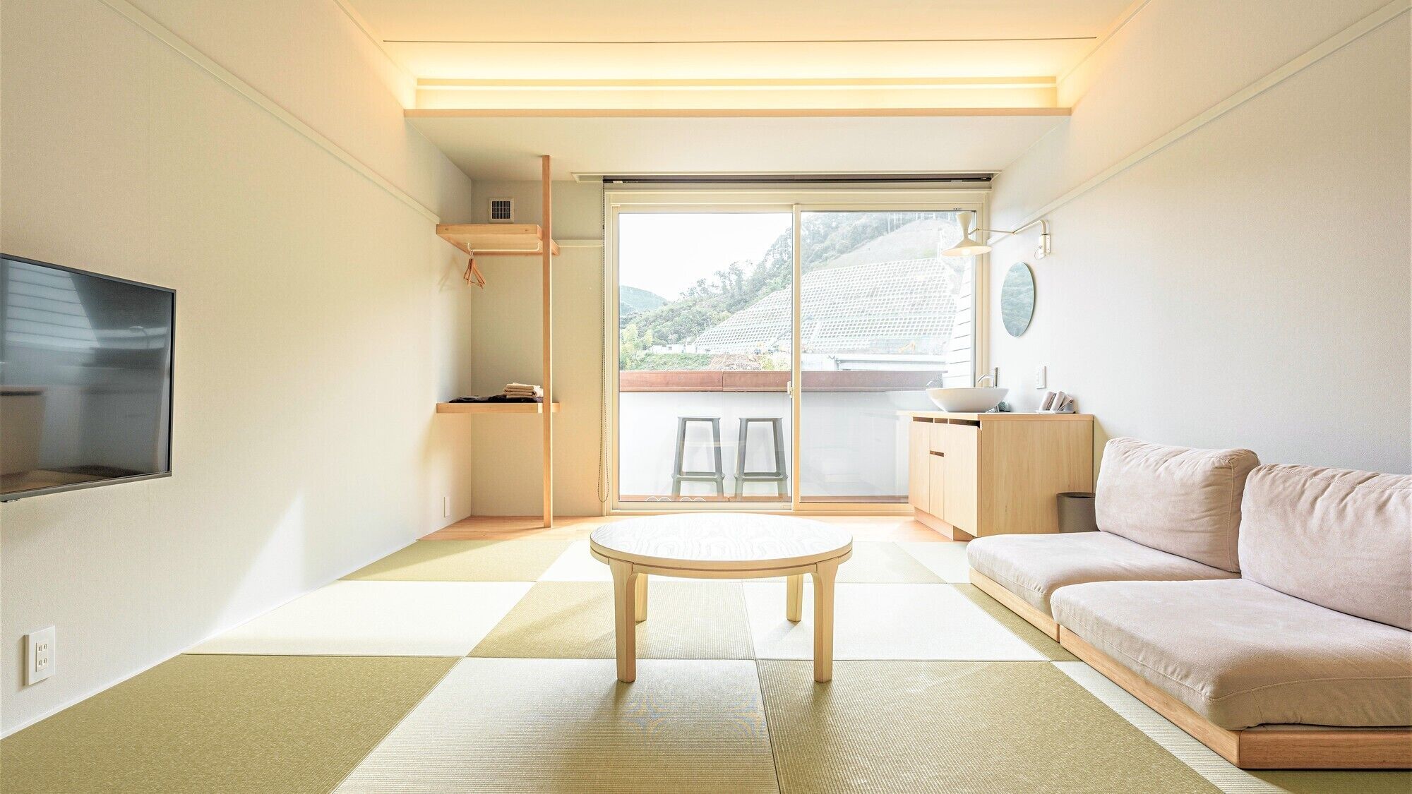 Una sala de estar minimalista con un sofá, una mesita, un televisor y un door corredizo que da a un balcón.