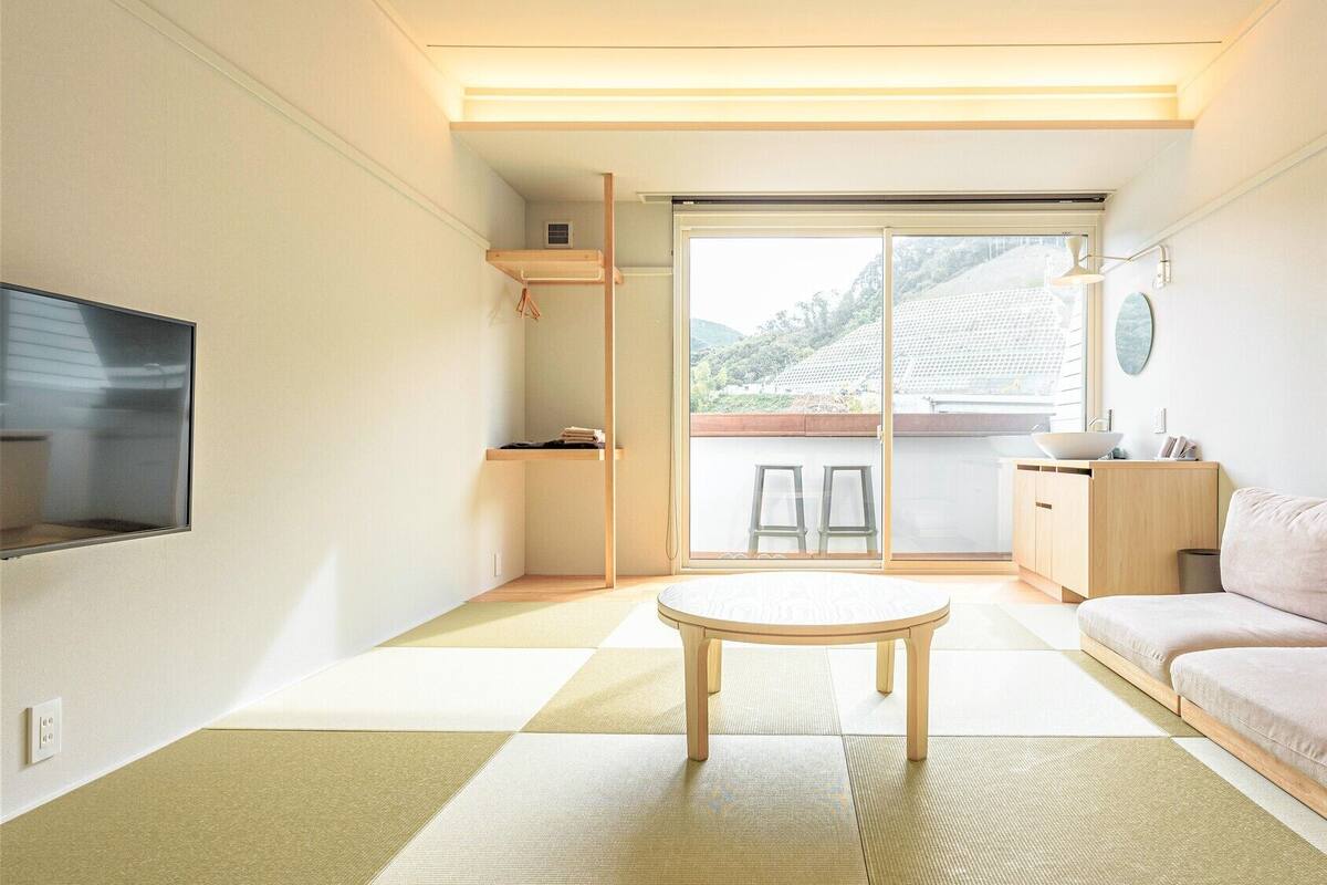 A minimalist living room with a sofa, a small table, a TV, and a sliding door leading to a balcony.